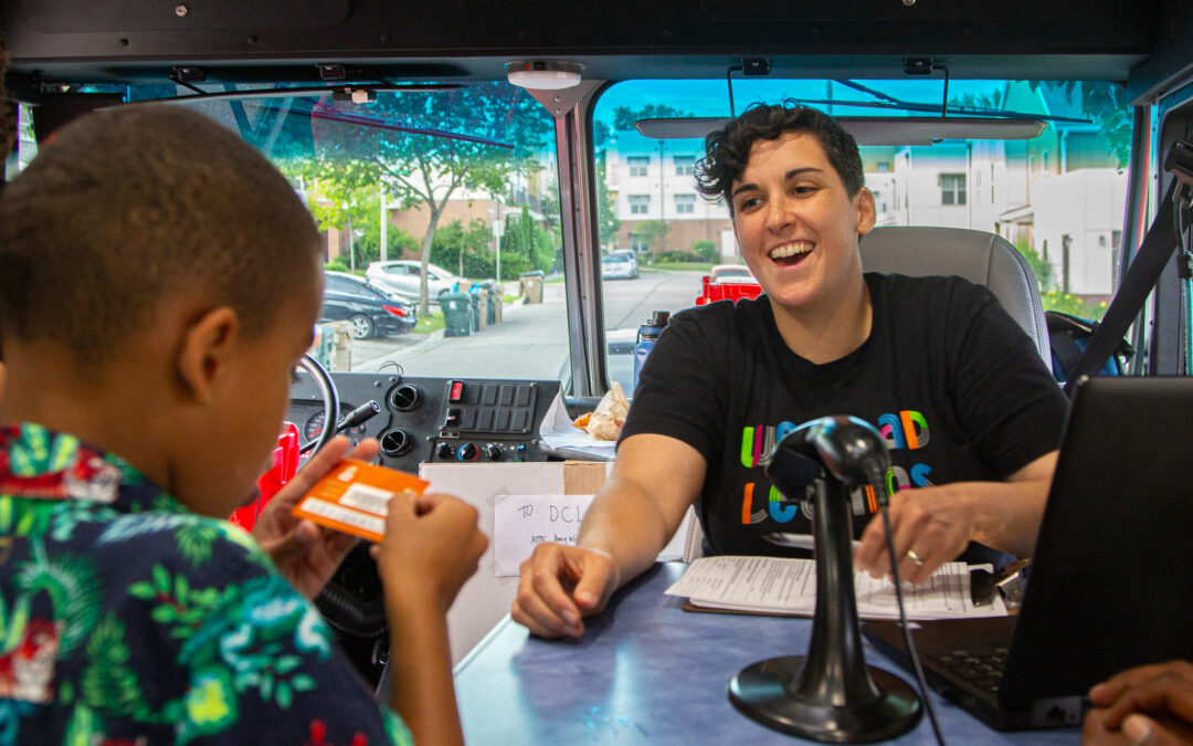 A child receives his library card on the Dream Bus from Library Assistant Amy Winkelman