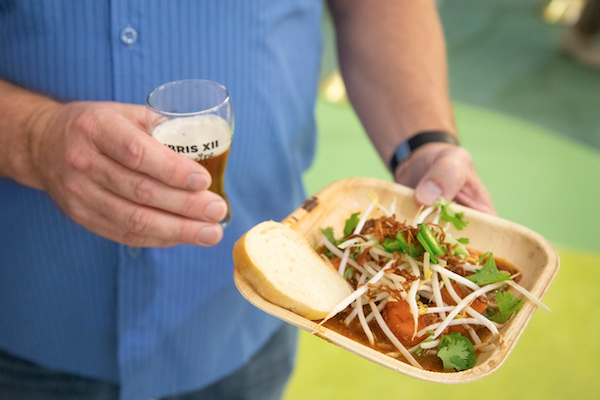 Ex Libris guest's hands holding a taster glass of beer and plate of food