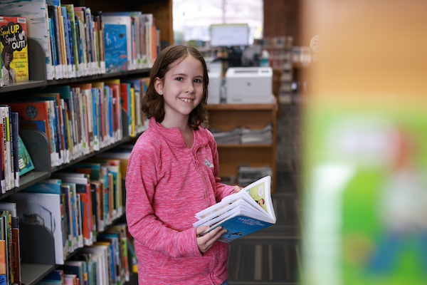 Smiling preteen girl holding a library book looking at camera